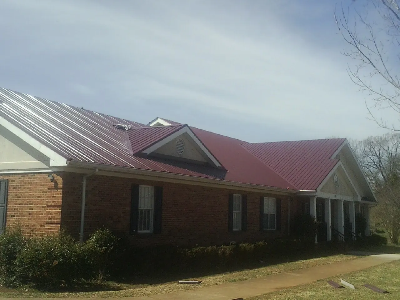Red metal roof with gabled entries on a long brick building, from a Hail Damage Roof Repair job in Oak Hill
