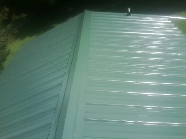 New green metal panels meeting at the ridge of a roof — Flat Roof Repair work by our crew in Oak Hill