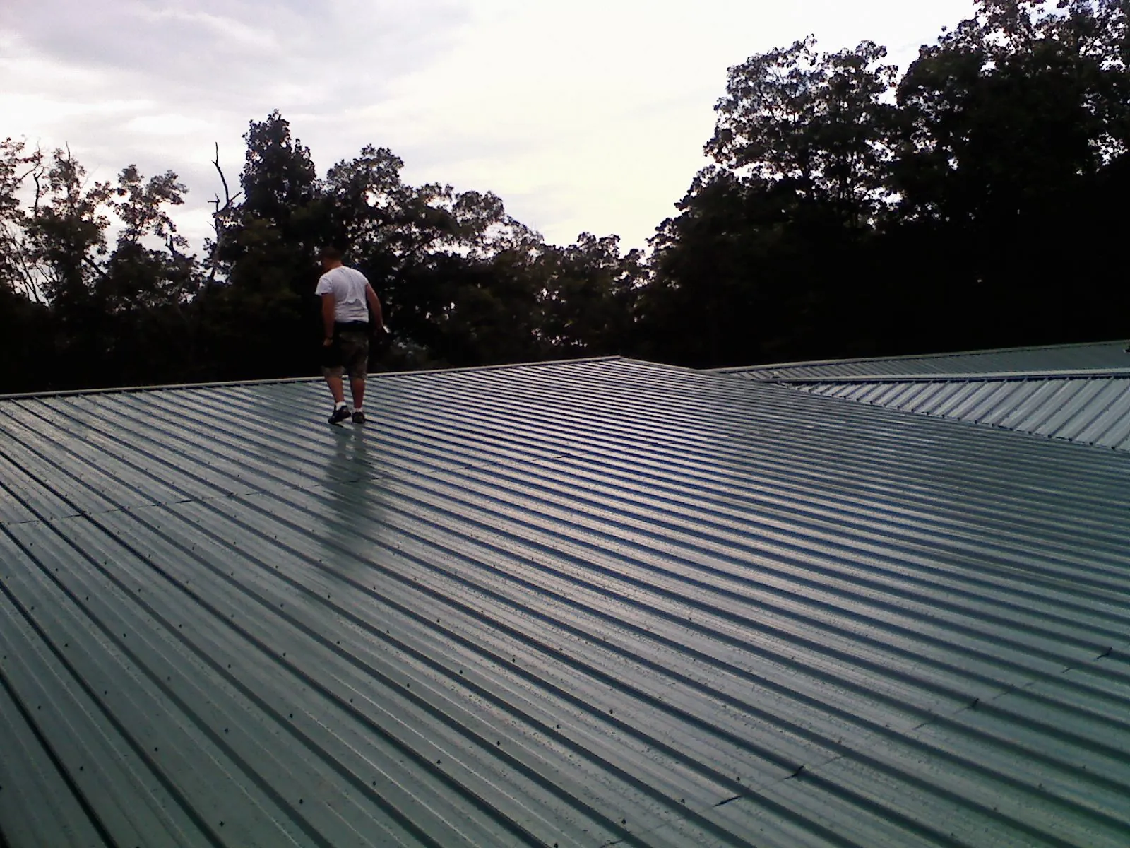Roofer walking a wide expanse of new green metal roofing in Oak Hill