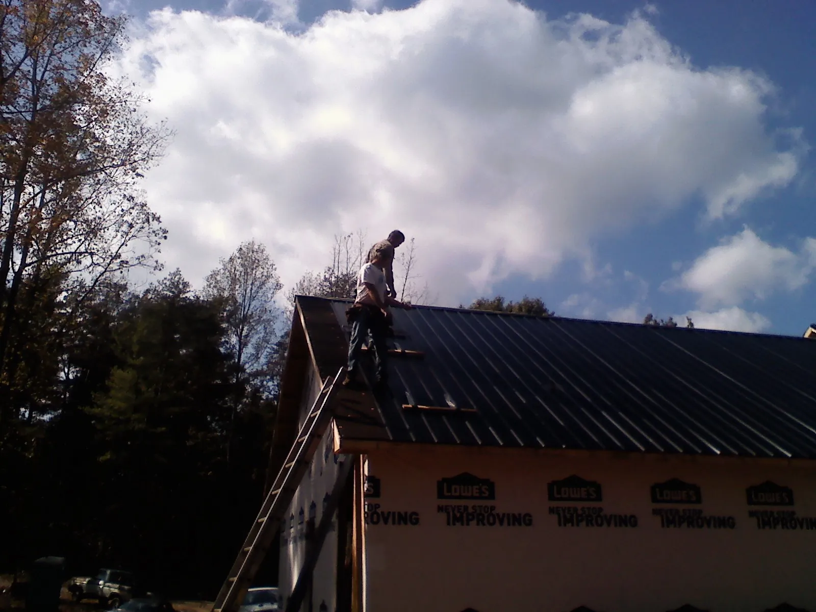 Roofer fastening dark metal panels high against a cloudy sky, from a Roof Inspection job in Oak Hill